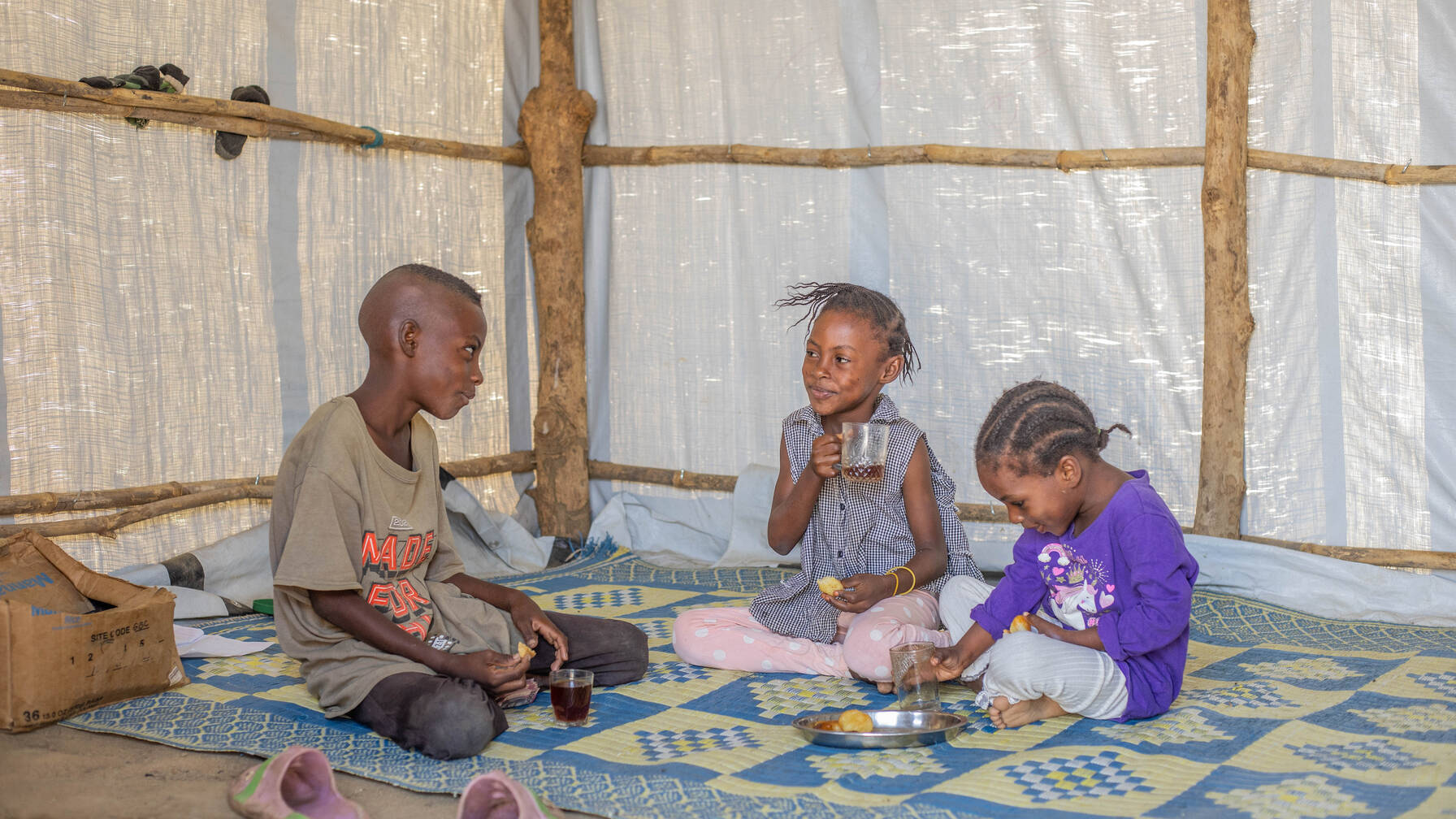 Zusammen mit ihrer Mutter und vier Geschwistern wohnt Arosula in einem einfachen Zelt im Gorom-Camp in Juba, Südsudan. Hier trinkt sie mit ihrem Bruder und ihrer Schwester.