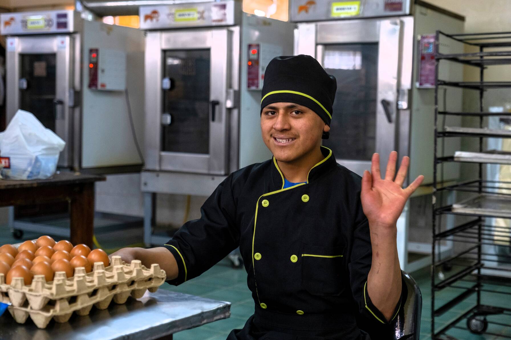 Un jeune homme est assis dans une cuisine et sourit à la caméra. 