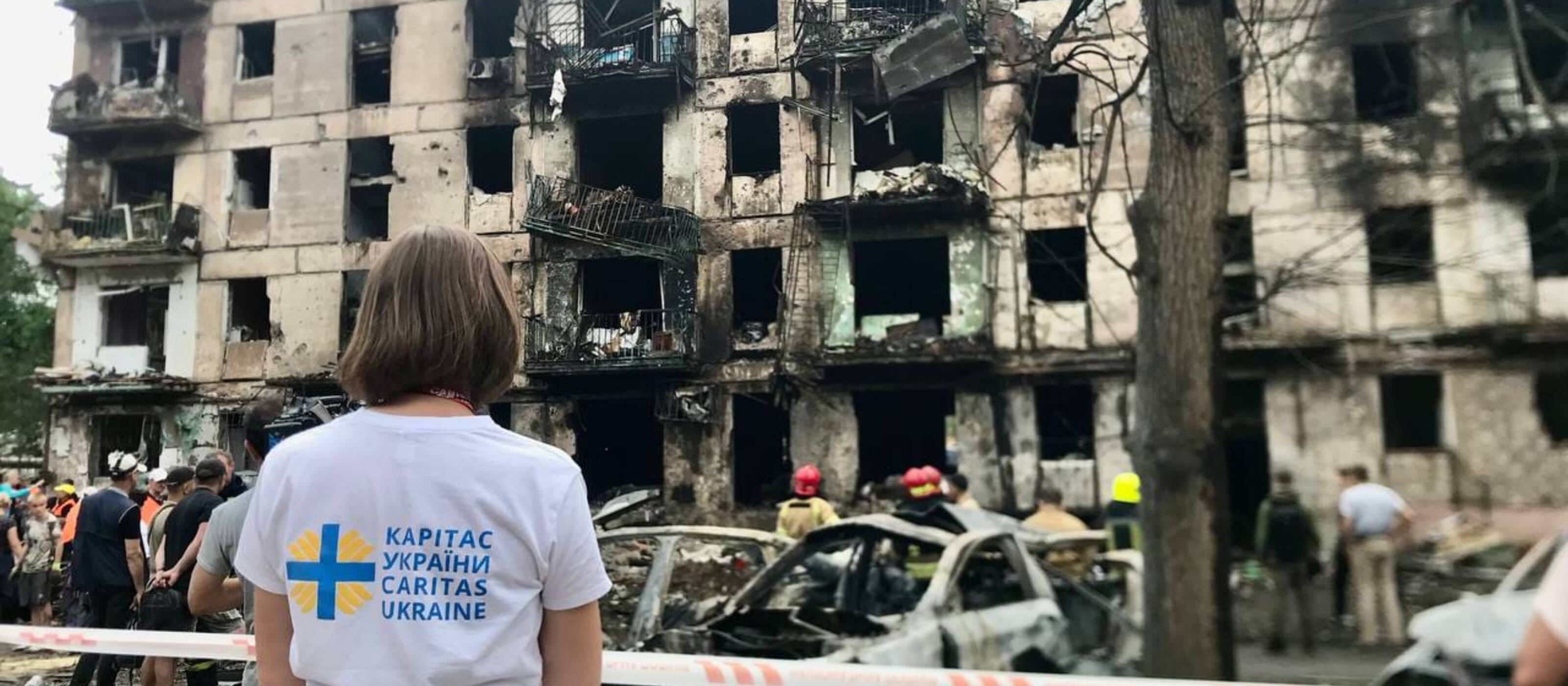 Mitarbeiterin von Caritas Ukraine steht vor zerstörtem Wohngebäude in Kryvyy Rih, Ukraine