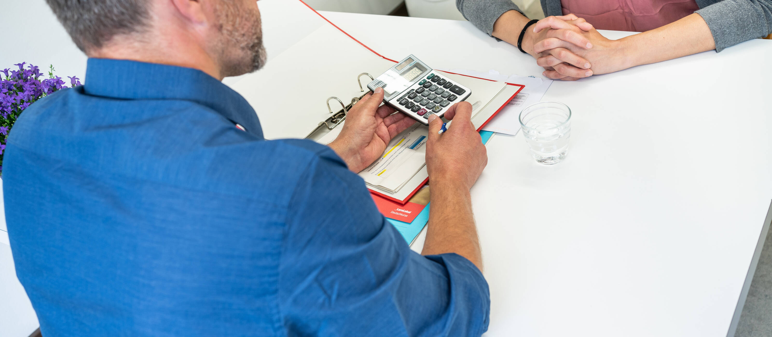 Un homme est assis à une table avec une femme et tient une calculatrice dans sa main. 