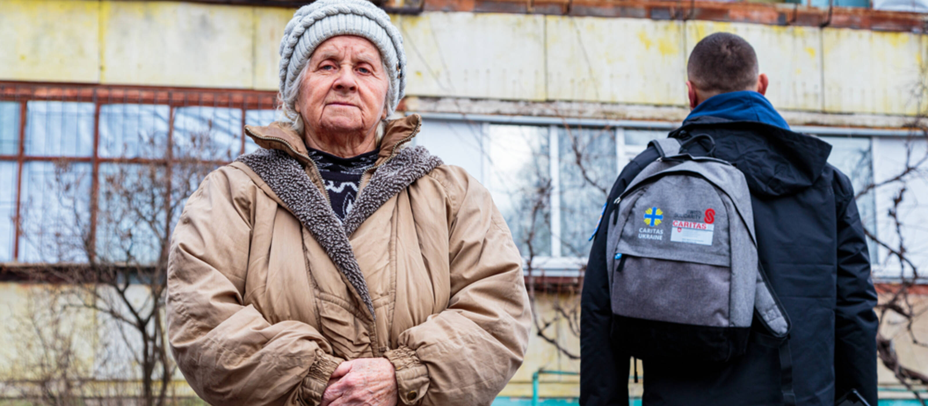 Une personne âgée ukrainienne et un collaborateur de Caritas Ukraine devant un bâtiment détruit.