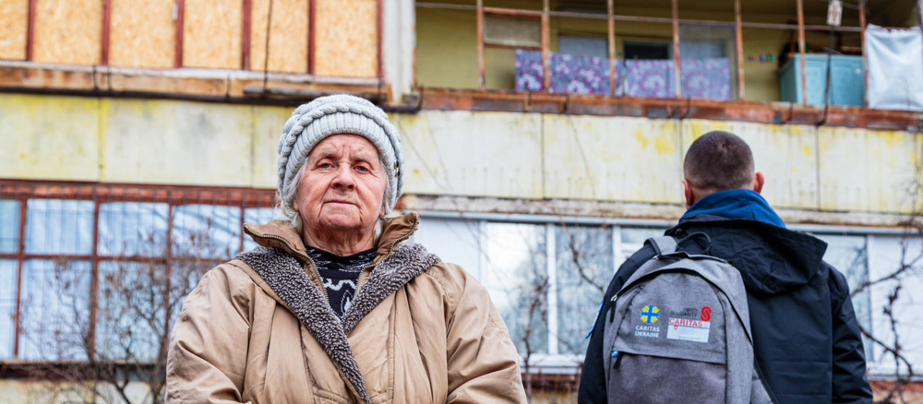 Une personne âgée ukrainienne et un collaborateur de Caritas Ukraine devant un bâtiment détruit.