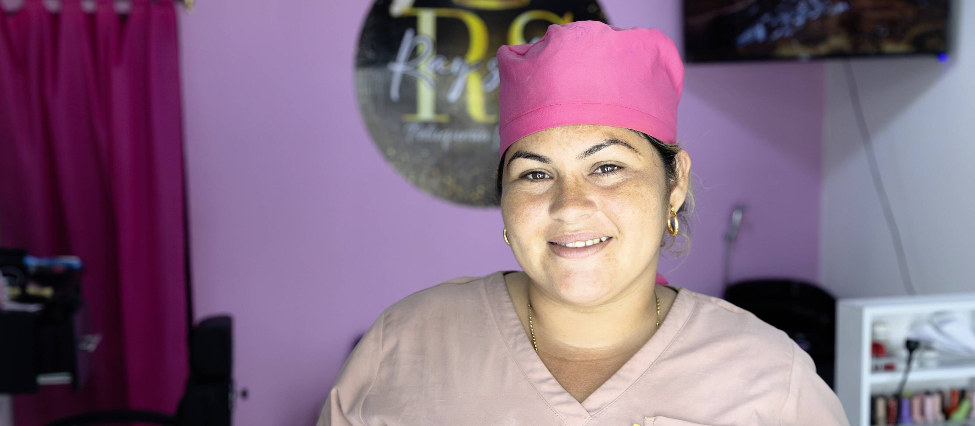 Une jeune femme se tient dans son salon de coiffure et regarde la caméra.