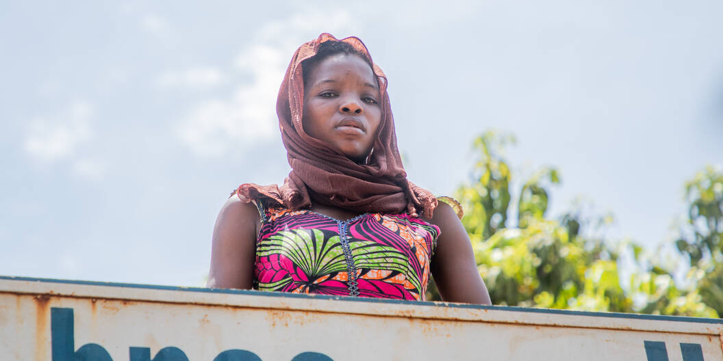 Eine junge Frau schaut von einem Hausdach runter direkt in die Kamera.